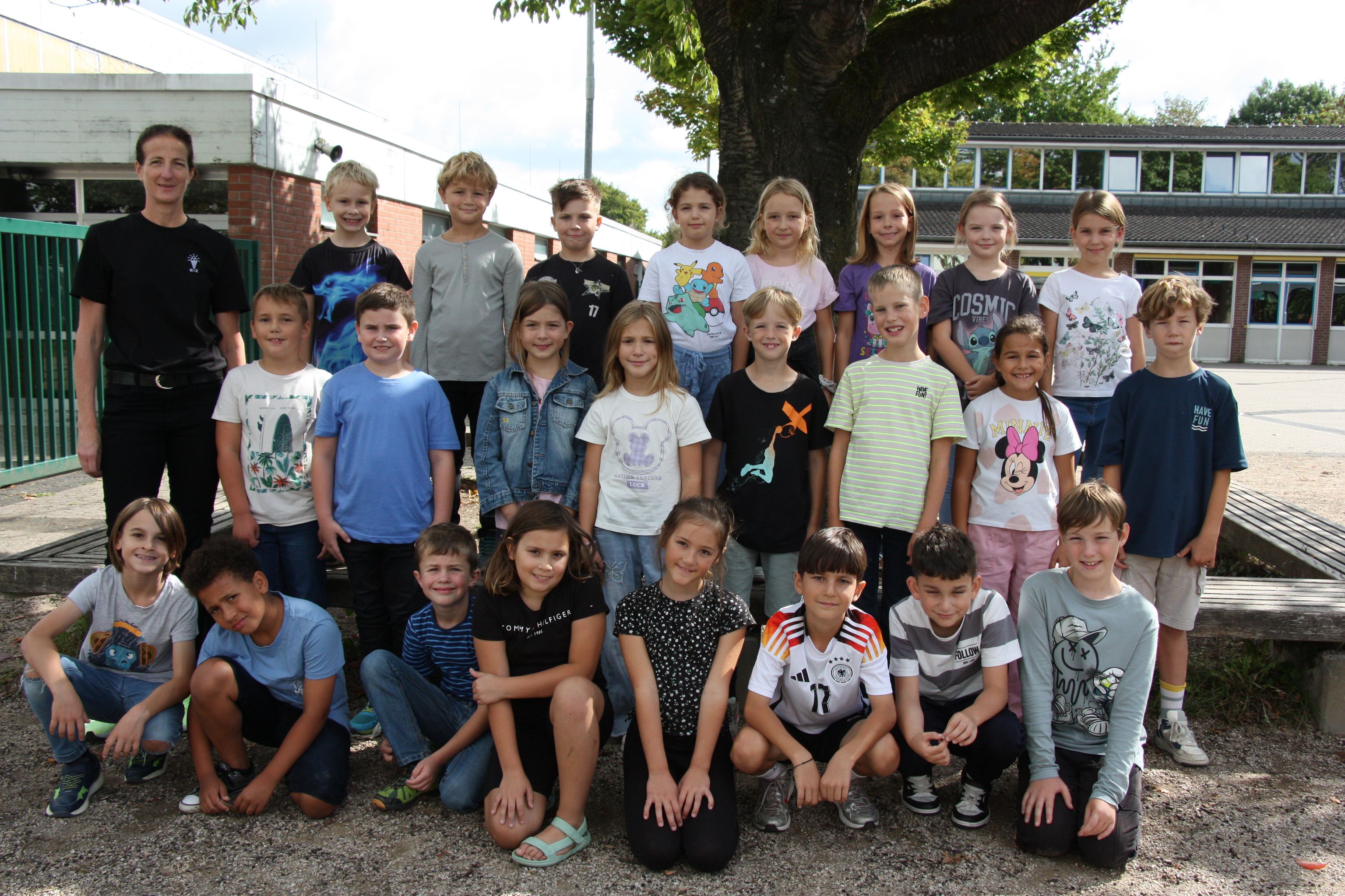 Gruppe von Kindern und einem Erwachsenen lachend vor Schule im Freien.