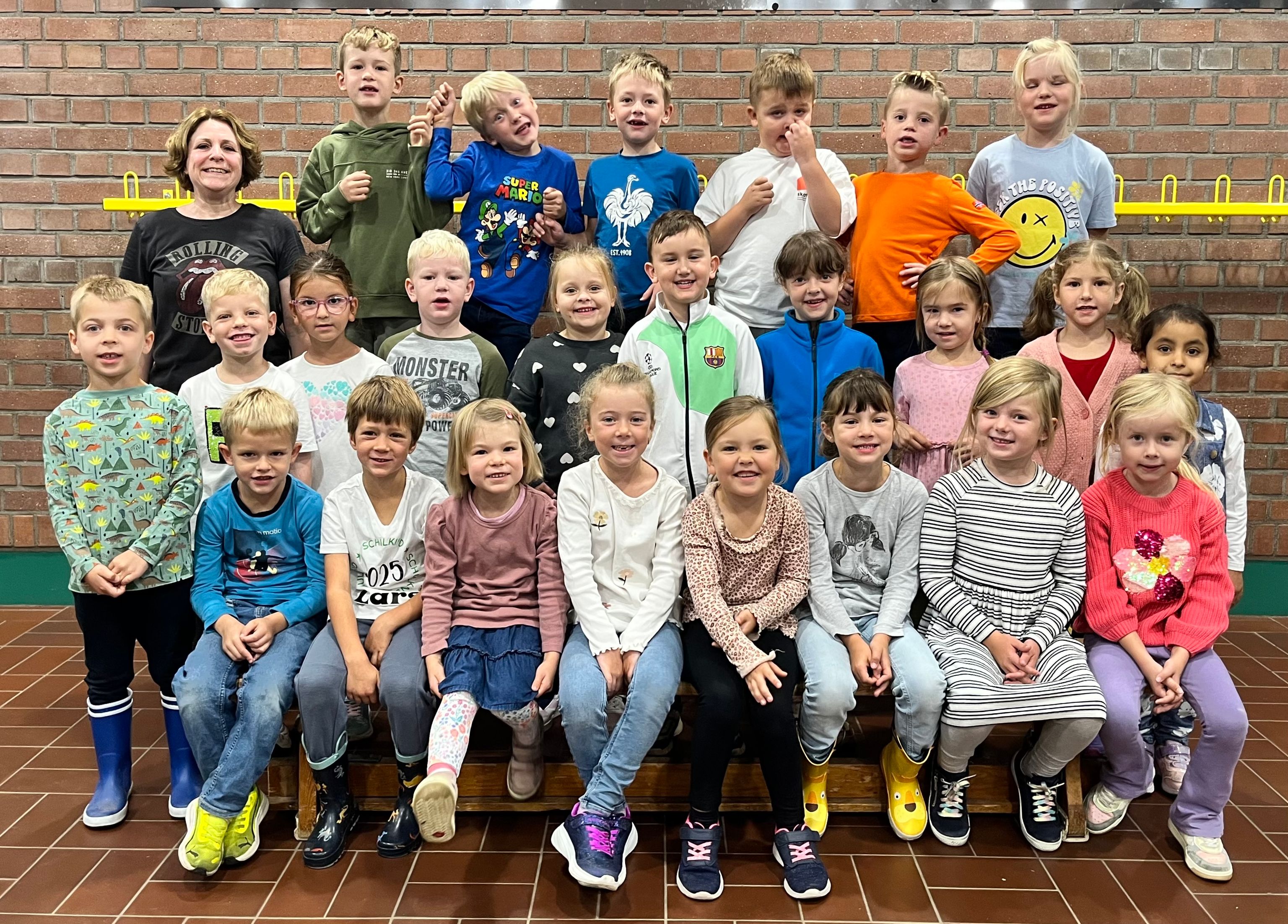 Gruppenfoto: Lehrerin mit fröhlichen Schulkindern vor Klassenzimmer.