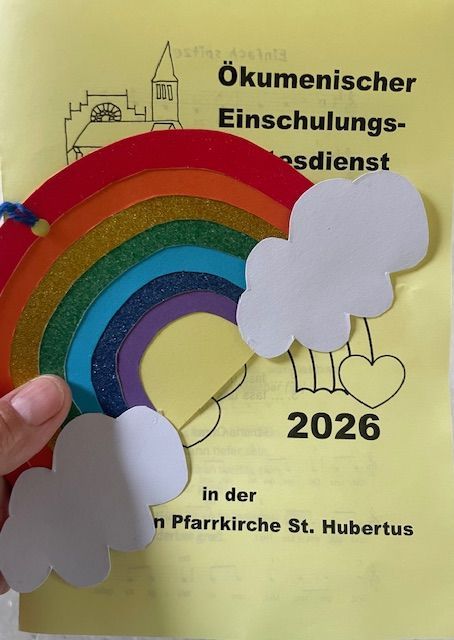 Einladungskarte für ökumenischen Einschulungsgottesdienst 2026 mit Regenbogen und Wolken.
