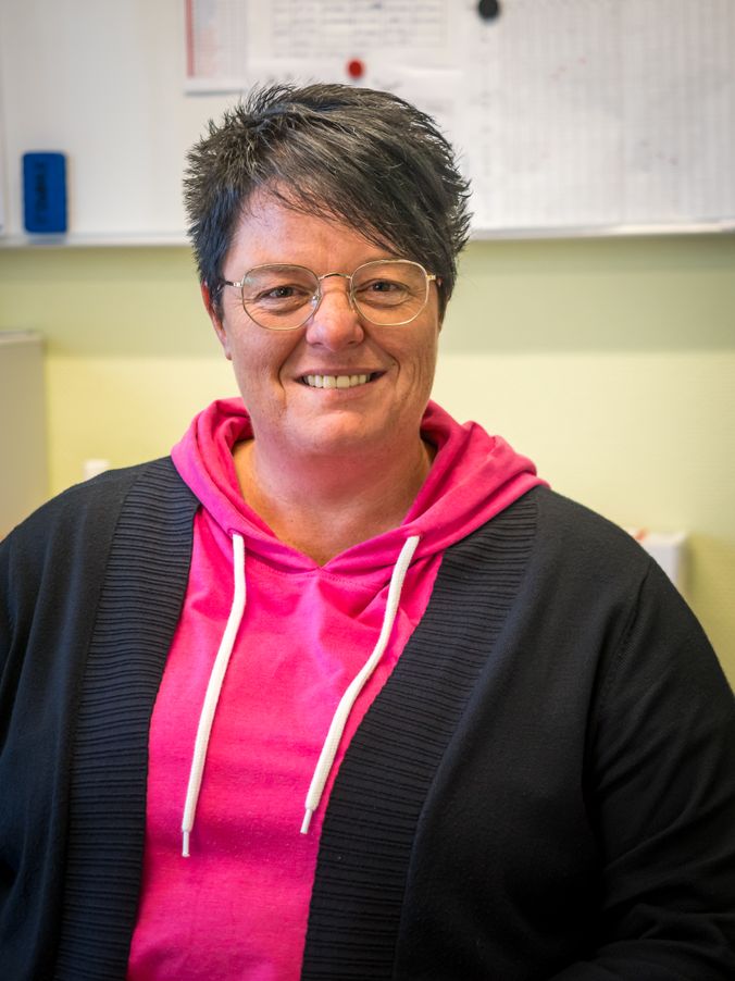 Lächelnde Person mit Brille in pinkem Hoodie und schwarzer Jacke.