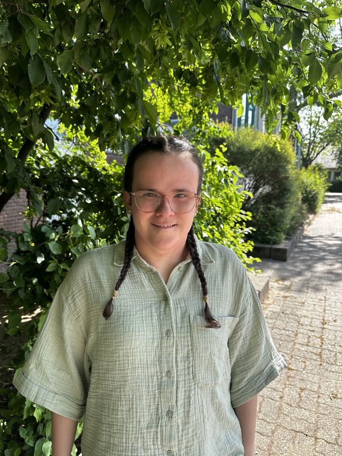 Lächelnder Mensch mit Dreadlocks vor grünen Pflanzen im Freien.